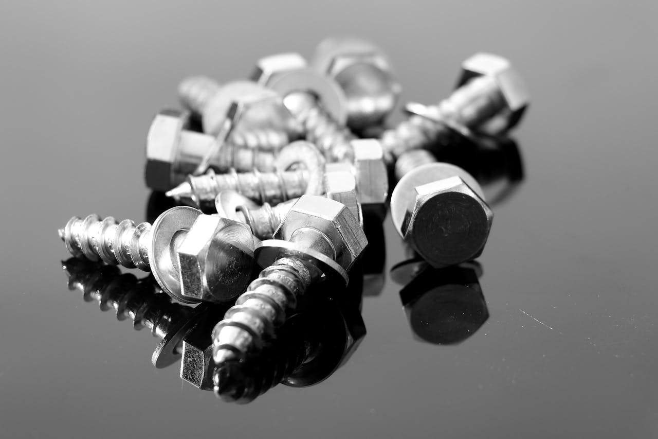 Close-up black and white photo of metal screws on reflective surface.